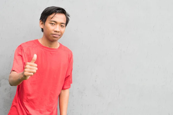 Indonesio Con Una Camiseta Roja Mostrando Pulgares Contra Una Pared —  Fotos de Stock