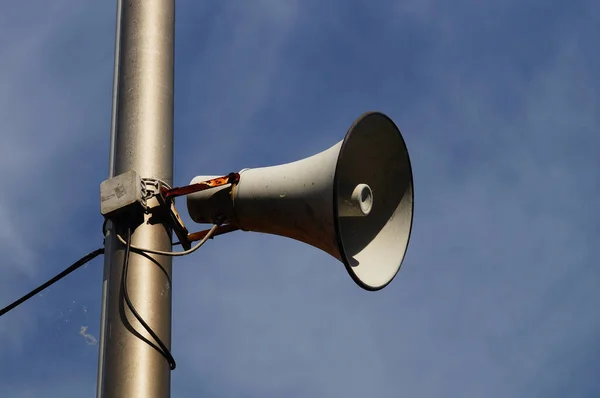 Emergency siren/call system at a petrol station. Loudspeaker on a pole against a cloudy sky.