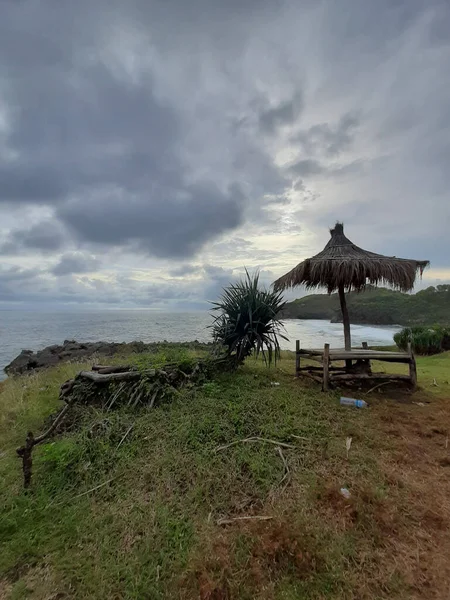 インドネシア ジャワ島のMidodarenラグーンビーチを望む緑豊かな岩の台地上に竹からパラソルと座っている場所 — ストック写真