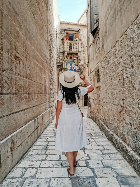 在克罗地亚田园诗般的特罗吉尔老城 穿着太阳帽和白色夏装走在石子路上的时髦年轻女子的后视镜 — 图库照片