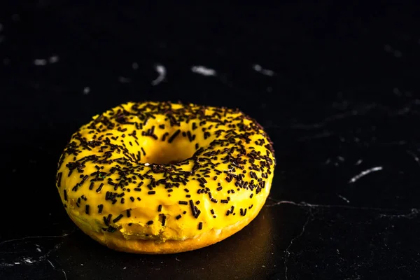 Una Rosquilla Amarilla Con Salpicaduras Sobre Fondo Negro — Foto de Stock