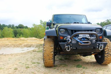 SLINDON, UNITED KINGDOM - Jun 25, 2021: A muddy off roader with big muddy tires equipped with bullbars rhino bars tow shackles and winch clipart