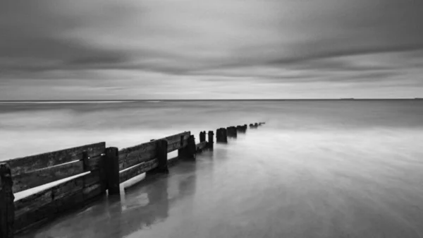 Grayscale Shot Calm Sea Wooden Wave Breaunder Cloudy Sky — Stock Photo, Image