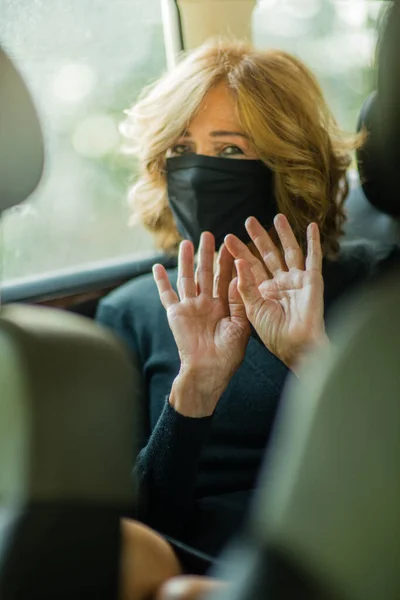 An elegant elderly woman wearing a face mask and refusing to take pictures on the car