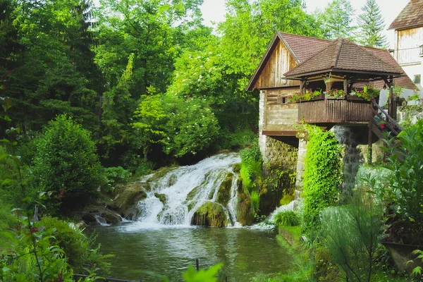一座房子 有一个小瀑布倾泻而下 流入被树木环绕的河流 — 图库照片