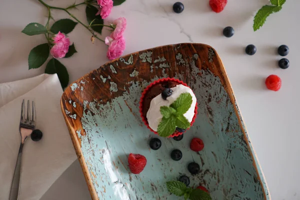 青い木の板の上に白いホイップクリームのチョコレートカップケーキのトップビュー — ストック写真