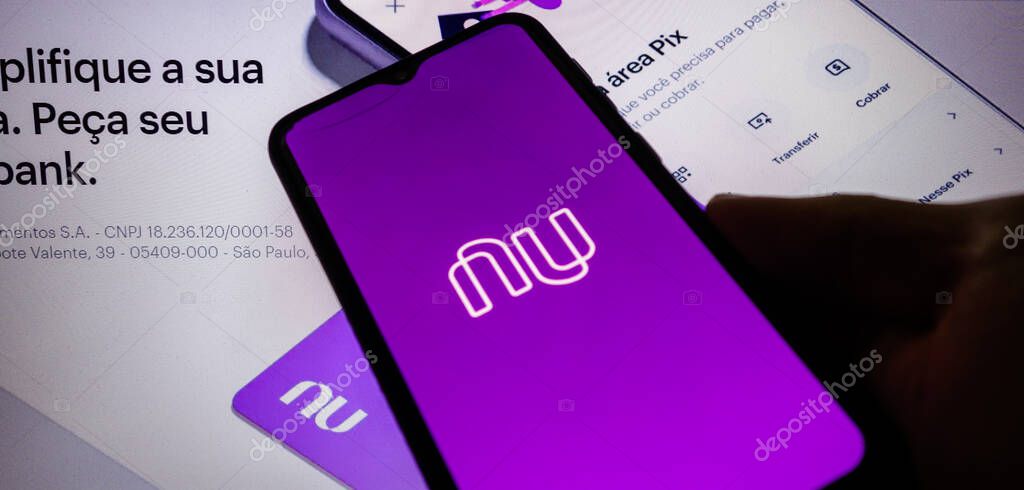 SAO PAULO, BRAZIL - Jul 03, 2021: Nubank brazilian fintech logo visible on smartphone screen, and website homepage on background