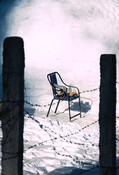A vertical shot of barbed wires and a chair in a snow-covered area