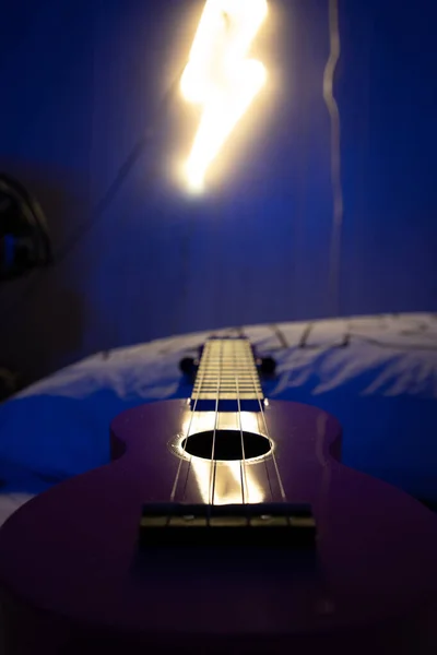 Tiro Vertical Ukulele Uma Cama Sob Luzes Com Fundo Embaçado — Fotografia de Stock