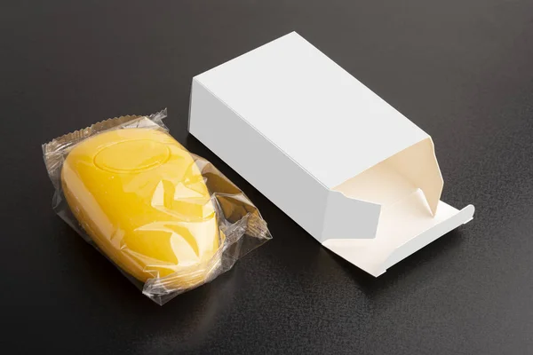一个开了的黄色肥皂旁边的白色空白盒在一个黑色表面可编辑的模型模板 — 图库照片