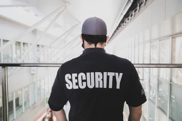 大きな窓のあるビルの中に黒いTシャツとキャップを着た男の警備員 — ストック写真