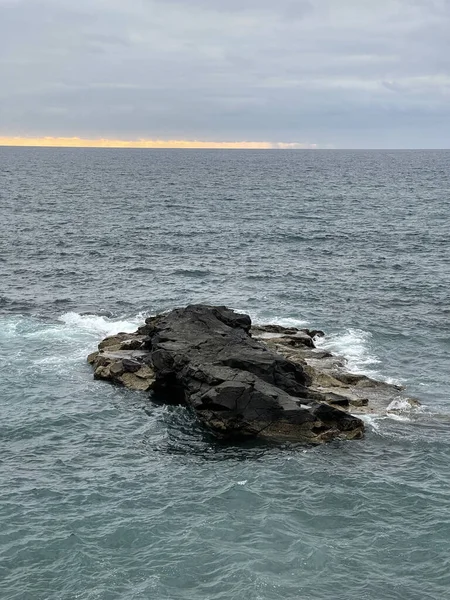 在阴沉沉沉的夕阳西下 在平静的大海中的一个小岩石岛 — 图库照片