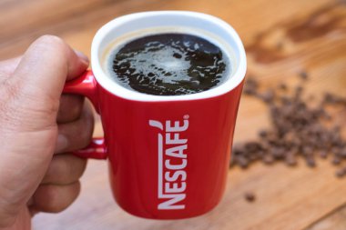 VOLOS, GREECE - Jul 12, 2021: A selective focus shot of a hand holding a red Nescafe (Nestle) mug with coffee clipart