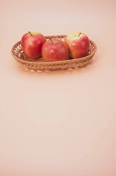 用粉红色背景与彩色空间隔开的在编织好的托盘上的新鲜苹果的垂直排列 — 图库照片