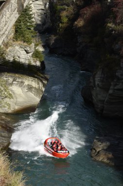 QUEENSTOWN, NEW ZEALAND - Jun 27, 2021: A Shotover jet boat speeding along the tight river clipart