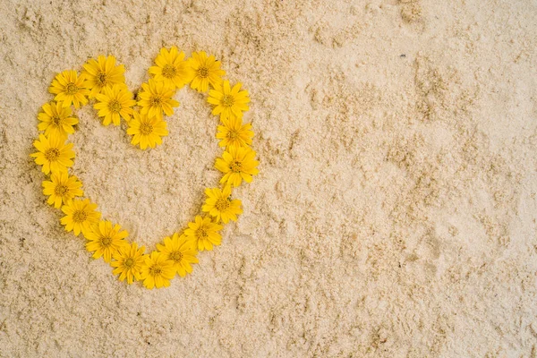 A top view of yellow flowers in the shape of a heart on a beige surface