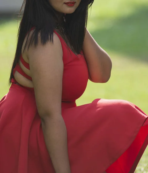 一个女性模特的竖直照片 穿着迷人的红色连衣裙 有侧面的坐姿 — 图库照片