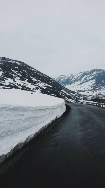Pionowe Ujęcie Mokrej Drogi Asfaltowej Otoczonej Małymi Wzgórzami Pokrytymi Śniegiem — Zdjęcie stockowe