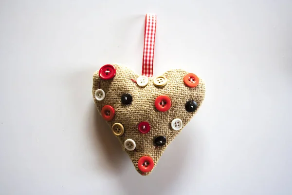 一颗可爱的心 用布制成 上面挂着纽扣 挂在一面普通的白墙上 — 图库照片