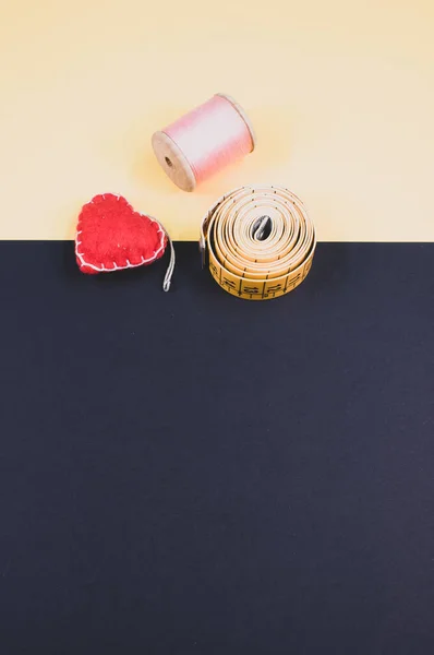 A flat lay of measuring tape, thread, and cushion on a beige and dark background with free space for text