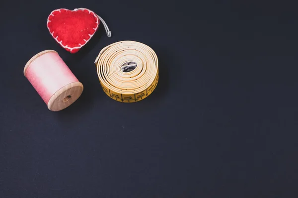 A flat lay of measuring tape, thread, and cushion isolated on a dark background with free space for text