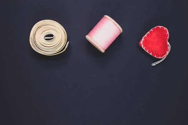A flat lay of measuring tape, thread, and cushion isolated on a dark background with free space for text