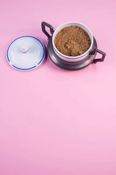 红糖粉红桌子上的一个小陶瓷罐子里的一块竖直的红糖 — 图库照片