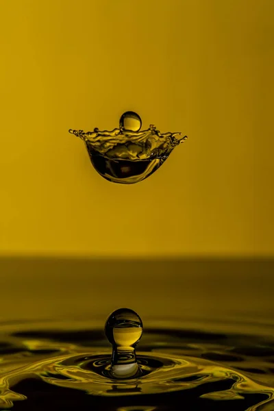 黄色の背景に水が飛び散る美しいショットと空気中の滴 — ストック写真