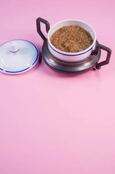 红糖粉红桌子上的一个小陶瓷罐子里的一块竖直的红糖 — 图库照片