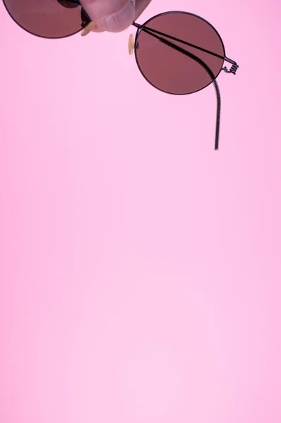 Pembe Arka Planda Güneş Gözlüğü Tutan Bir Elin Dikey Görüntüsü — Stok fotoğraf