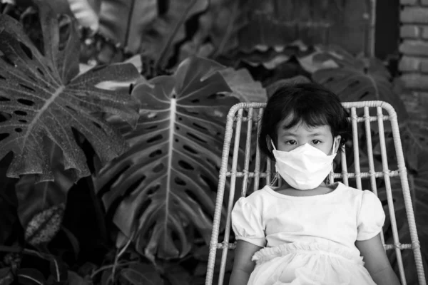 一张亚洲小女孩头戴面罩坐在椅子上的灰白照片 — 图库照片