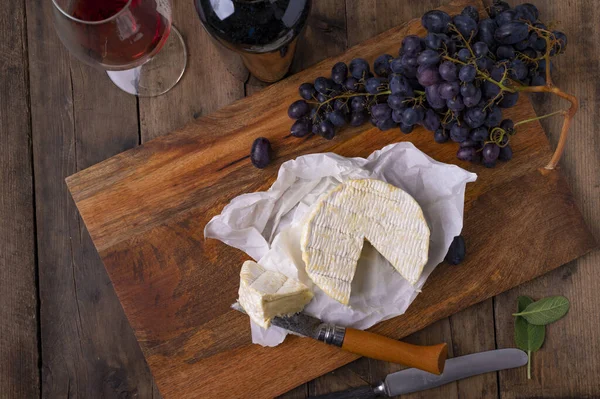 一块切好的奶酪和葡萄 放在木板上 还有一杯葡萄酒 — 图库照片