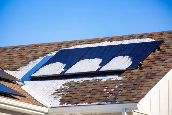 A snowy rooftop with tiles and solar panel on it