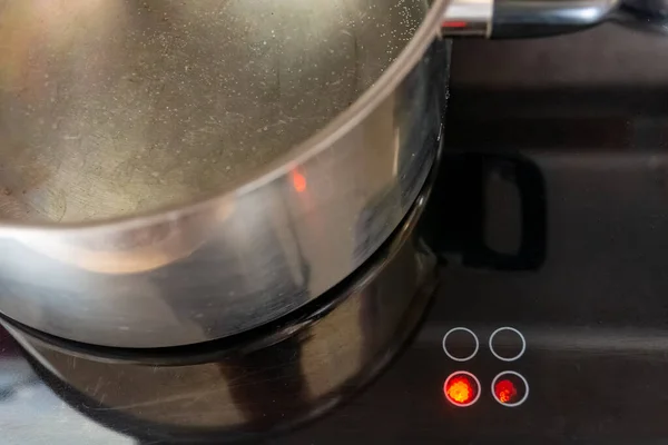 火锅在现代火炉上烹调的金属锅 其反光和红色圆点表示它下面的热 — 图库照片