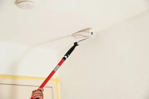 A low angle shot of a person painting the ceiling with a long brush