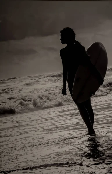 一个荷兰角度拍摄的女冲浪者在海浪中抱着冲浪板的轮廓 — 图库照片