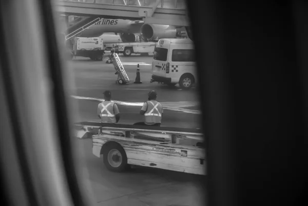 从飞机窗上看到的机场坡道上有地面人员和车辆的灰度照片 — 图库照片