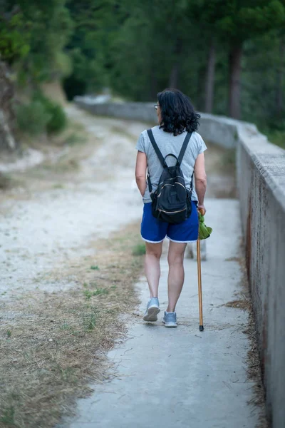 棒で公園を歩くバックパックを持つ女性の垂直ショット — ストック写真