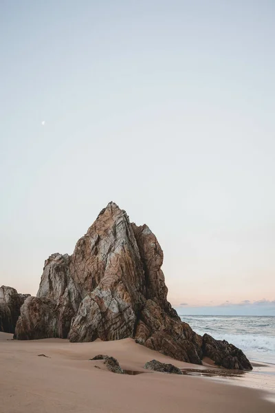 夕阳西下岩石悬崖峭壁的田园诗般的沙质海岸的垂直拍 — 图库照片