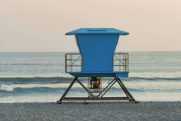 日落时沙滩上一座蓝色的救生塔的风景画 — 图库照片