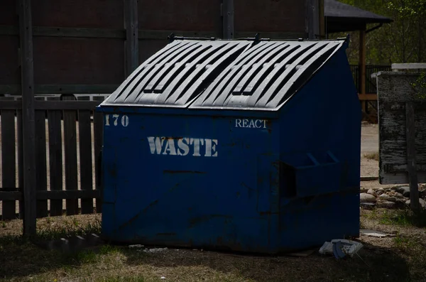 Zbliżenie Niebieskiego Metalowego Koszyczka Śmieci Przed Drewnianym Płotem Domu — Zdjęcie stockowe