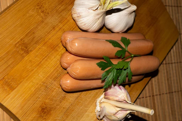 An overhead shot of smoked sausages with garlic bulbs on a wooden board