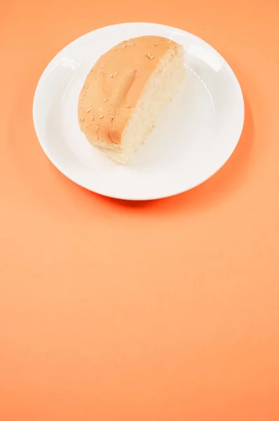 Вертикальний Знімок Наполовину Хлібної Булочки Тарілці Ізольовано Світло Оранжевому Фоні — стокове фото