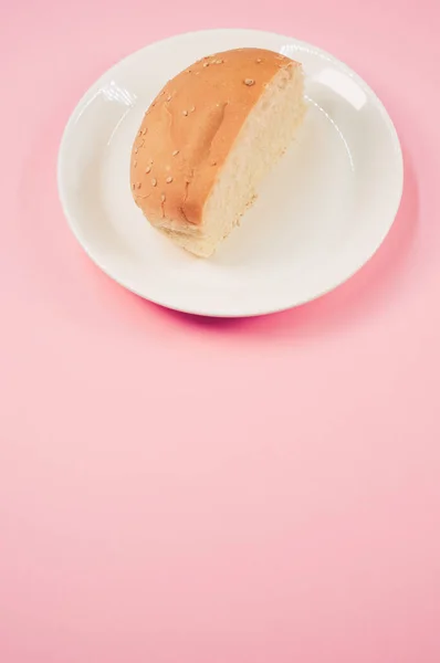 Вертикальний Знімок Наполовину Хлібної Булочки Тарілці Ізольовано Рожевому Фоні — стокове фото