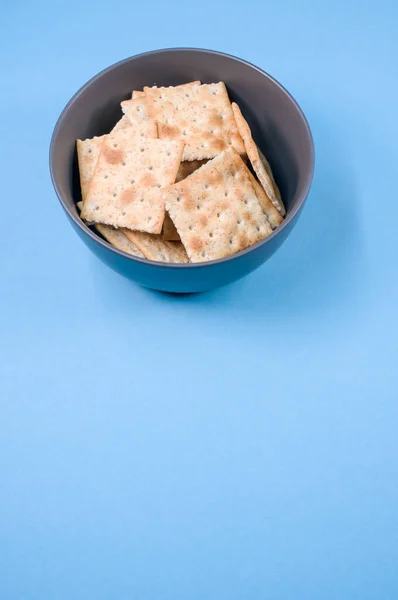 在蓝色背景隔离的碗上垂直拍摄的正方形饼干 — 图库照片