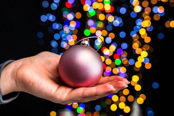カラフルなボケの照明を背景にクリスマスの飾りを持つ手 — ストック写真