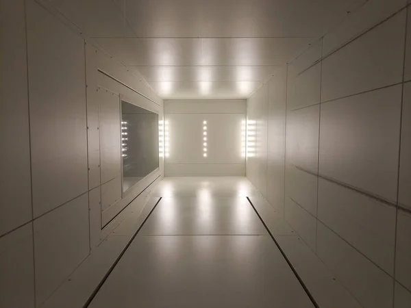 A white futuristic hallway with bright lights shining at the end of it