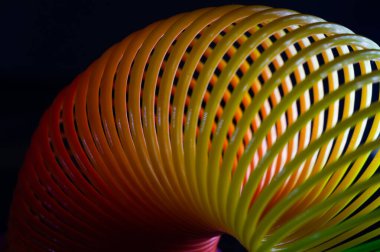 A closeup shot of a slinky rainbow spring toy on a black background clipart