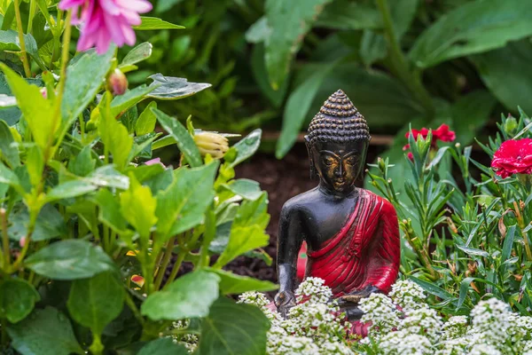 在被不同植物环绕的花坛上的黑色佛像的一张照片 — 图库照片