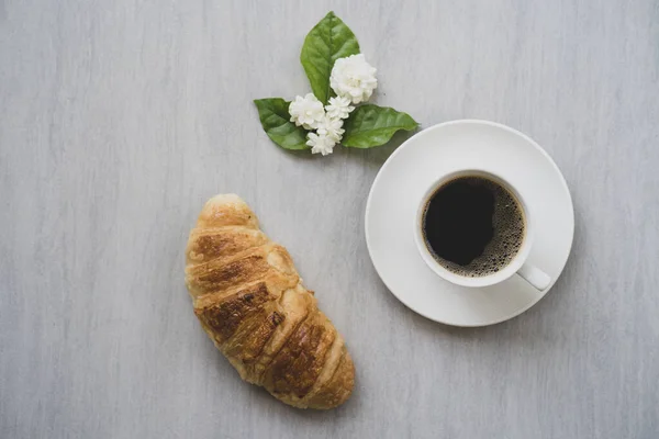 一张特写的羊角面包 一杯咖啡和桌上的茉莉花 — 图库照片